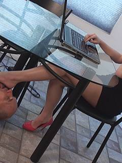 Bald slave is under the table: licking girl's soles while she is busy working on the computer