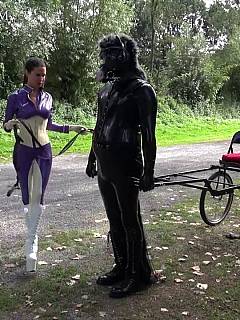Ponyboy in full-body rubber costume is spending day out in the field riding his mistress on a chariot